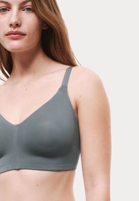 Grå sömlös behå med V-ringad design, justerbara band, slät yta och subtila sömnadsdetaljer, bärs av en modell.