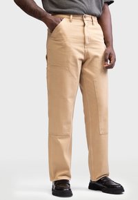 Beige cargo bukser med en afslappet pasform, der har store sidelommer, kontrastsygning og et robust bomuldsmateriale.