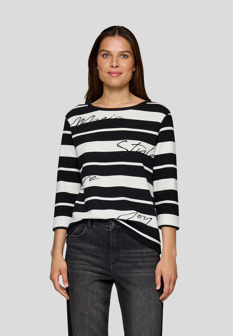 Schwarz-weißer gestreifter Langarm-Top mit Rundhalsausschnitt und geschriebene Akzente. Der Stoff wirkt weich mit einer lockeren Passform, kombiniert mit dunklen Jeans.