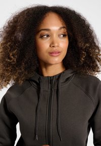 Mörkgrå zip-up hoodie med dragsko och en mjuk textur. Har raglanärmar och en åtsittande halsringning. Enkelt design utan mönster.