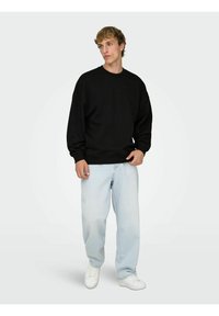 Felpa nera in cotone con scollo rotondo e maniche lunghe, abbinata a jeans di denim azzurri e sneakers bianche. Design semplice.