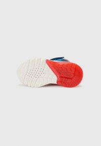 Sneaker-Außensohle aus strukturiertem, weißem Gummi, mit roten Akzenten und einem Profilmuster. Sie zeichnet sich durch ein gewölbtes Design für verbesserten Halt und Flexibilität aus.