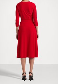 Robe rouge longueur genou en tissu lisse, avec manches trois quarts et taille cintrée, dotée d'une jupe évasée.