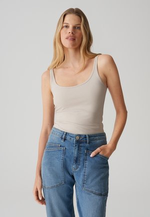 Lichtbeige tanktop met een ronde hals, gecombineerd met hoog- taille blauwe spijkerbroek. De spijkerbroek heeft grote patch zakken en een lichte vervaging.