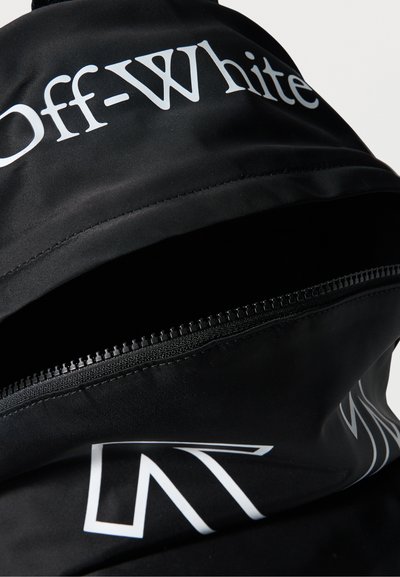 Μαύρο ύφασμα με το κείμενο "Off-White" σε λευκό και ένα μαύρο φερμουάρ που είναι μερικώς ξεκουμπωμένο σε μια τσάντα ή ένδυμα.