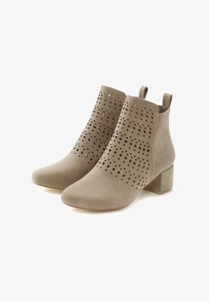 Botas de tobillo beige con patrones geométricos cortados, material de ante suave, punta afilada y un tacón bajo en bloque. Cuenta con lengüetas de agarre en la parte posterior.