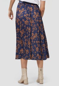 Marinblå plisserad kjol med brunt blommönster, elastisk midja och längd till mitten av vaden, matchad med krämfärgade ankelskor med klack.