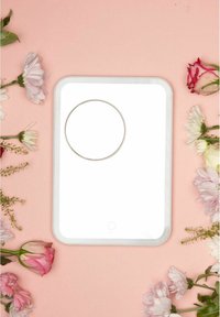 White LED mirror with a circular ring in the center, enclosed in a smooth plastic frame, surrounded by assorted flowers on a pink background.