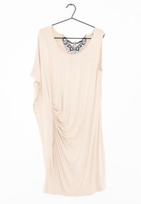 Robe beige drapée en tissu doux, avec un col rond orné de dentelle noire et de doux plis sur un côté. Accrochée à un crochet noir.