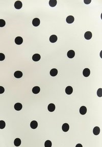 Tissu blanc avec de petits pois noirs régulièrement espacés formant un motif régulier sur toute la surface.