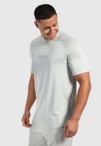 Jasnoszara, krótko rękawowa koszulka sportowa o teksturowanej powierzchni i logo. Posiada okrągły dekolt i rękawy raglanowe, co zapewnia swobodę ruchów.
