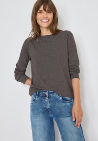 Camicia a maniche lunghe a righe marroni con scollatura rotonda, abbinata a jeans in denim blu chiaro con chiusura a doppio bottone e vestibilità slim.