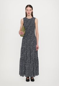 Mustassa kukkakuosisessa maksimekossa on tiukka vartalonmyötäinen bodice ja liehuva hame. Valmistettu kevyestä kankaasta, jossa on pieniä sinisiä kukkia ja hihaton muotoilu.