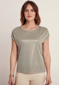 Top a maniche corte di colore verde chiaro, realizzato in tessuto lucido con una sottile texture e maniche arrotolate, caratterizzato da un collo rotondo e una vestibilità comoda.