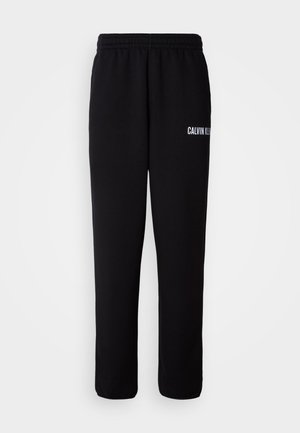 Pantaloni de trening negri cu talie elastică, având un logo alb "CALVIN KLEIN" pe piciorul stâng. Țesătură moale și o croială lejeră.