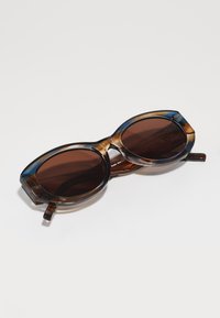 Lunettes de soleil en écaille de tortue avec des verres ronds marron, dotées de montures épaisses et d'accents angulaires, offrant un design audacieux et moderne.