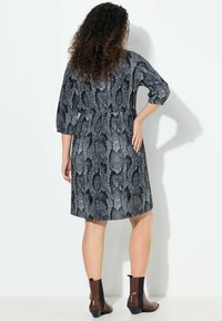 Robe imprimée avec un motif de peau de serpent noir et blanc, manches trois-quarts, taille cintrée et ourlet à la hauteur du genou. Bottines marron.