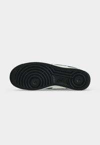 Suola in gomma nera di una sneaker Nike con motivi circolari del battistrada e il logo Nike impresso al centro.