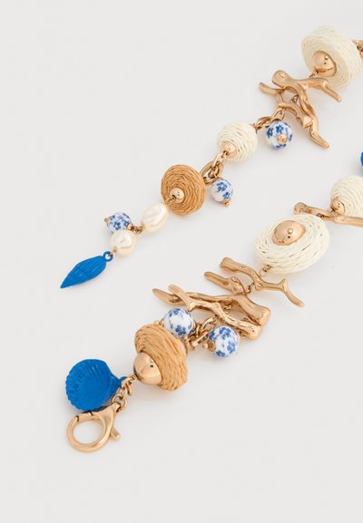 Βραχιόλι με συνδέσμους σε χρυσαφί απόχρωση σε σχήμα κοραλλιού, μπλε και λευκές λουλουδάτες χάντρες, πλεγμένους μπεζ κρίκους, μαργαριτάρια και μπλε χάντρες σε σχήμα φύλλου και κοχυλιού σε λευκό φόντο.