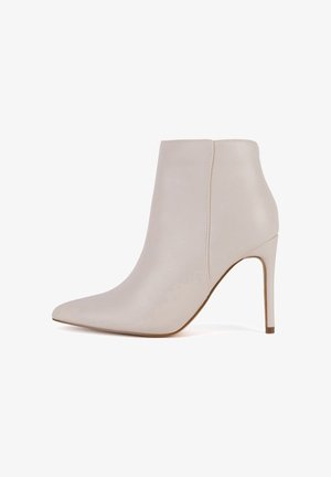 Bēša ādas potītes zābaki ar smailu purngalu un stiletto papēdi. Gluda tekstūra, vienkāršs dizains bez redzamām rotāšanām vai rakstiem.