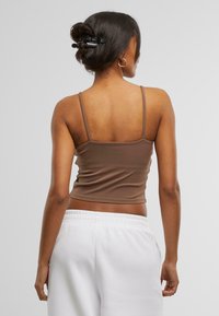 Smeđi krojeni crop top od glatke tkanine, s tankim naramenicama. Stražnji dio je minimalistički s jednostavnim dizajnom, uparen s bijelim trenirkama.