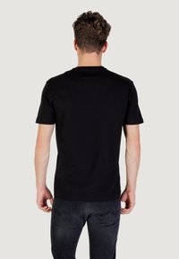 Camiseta negra de manga corta de algodón, con cuello redondo y una textura simple y suave. La vista trasera no muestra patrones o logos distintivos.