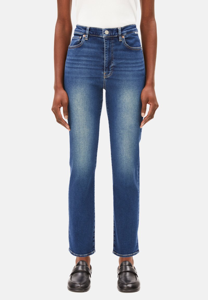 Jeans bleu taille haute en denim, présentant une silhouette ajustée, cinq poches, un léger effilochage sur les cuisses et un ourlet net.