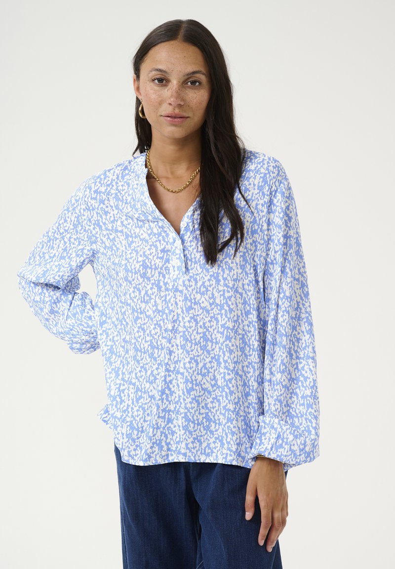 Chemise à manches longues bleu clair avec un motif abstrait blanc, col classique et coupe décontractée. Le tissu semble lisse et léger.