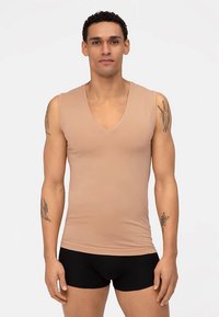 Lichtbeige mouwloze tanktop met v-hals, gemaakt van gladde stof. Heeft een aansluitend ontwerp, gedragen met zwarte korte broek. Geen zichtbare patronen of accenten.
