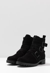 Botines de ante negro con tres correas ajustables, un zipper lateral y una suela de goma texturizada. Diseño resistente con un tacón ligeramente grueso.