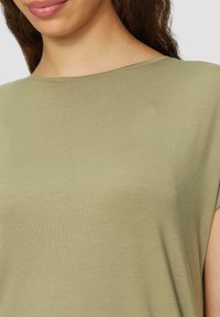 Oliwkowy t-shirt wykonany z miękkiej, gładkiej tkaniny. Posiada szeroki, zaokrąglony dekolt i krótkie rękawy. Prosty, minimalistyczny design.