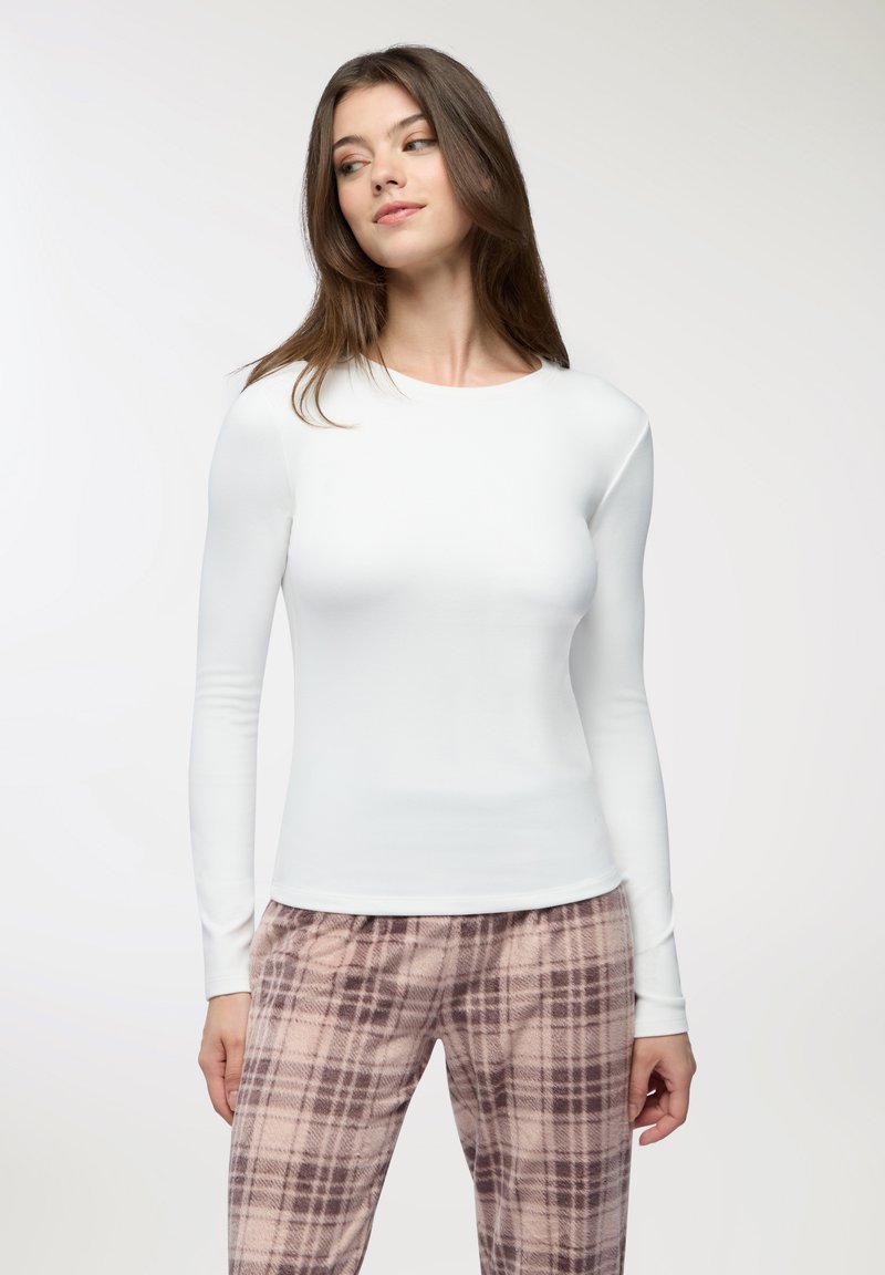 T-shirt bianca a manica lunga con scollo rotondo, realizzata in tessuto morbido, abbinata a pantaloni a quadri con motivo rosa e marrone.
