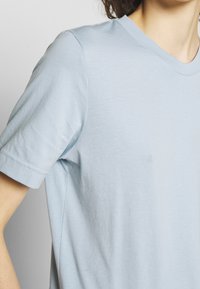 Camiseta de algodón azul claro con un corte relajado, mangas cortas y un sencillo diseño de cuello redondo. Textura suave, sin patrones ni acentos visibles.