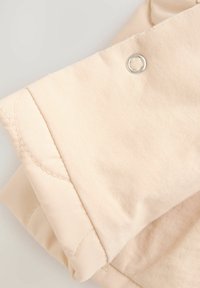 Beiger Stoff mit glatter Textur und gesteppten Details, mit einem Metalleyelet. Das Design umfasst geschichtete, gefaltete Elemente.