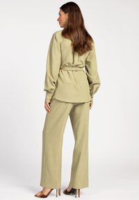 Light olive green, textured fabric blouse with a relaxed fit, cinched waist, and long sleeves, paired with wide-leg trousers and high heels.