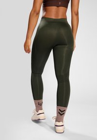 Leggings verde oliva con una cintura alta, paneles texturizados y un diseño ajustado. Combinados con zapatillas de deporte de color claro y calcetines con estampado.