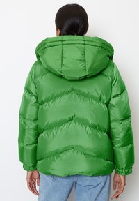 Green puffer jacket with a hood, featuring a shiny texture and horizontal stitching detail. Ribbed cuffs with a slight balloon shape.