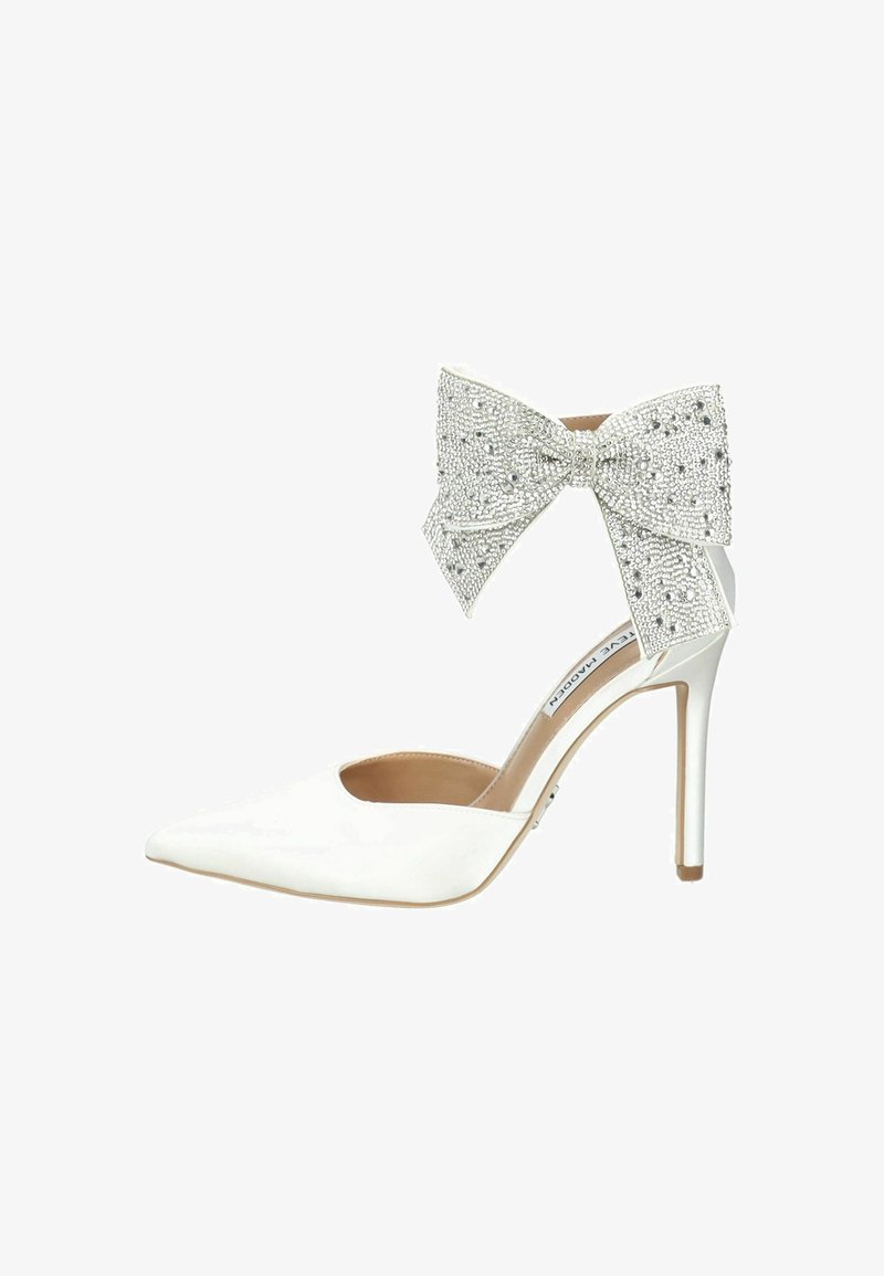 White high-heeled shoe with a pointed toe and open side. Features a large, crystal-embellished bow at the ankle. Smooth leather finish.