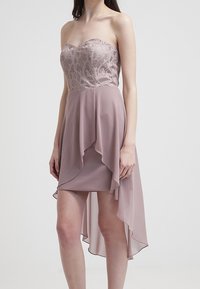Bezramenné šaty v lilkovém odstínu s propracovaným krajkovým korzetem, splývavou šifónovou sukní a asymetrickým lemem. Vyznačuje se jemnou texturou a delikátními detaily.
