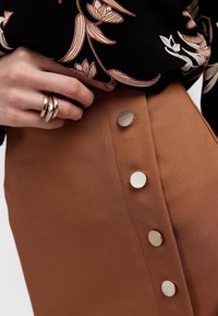 Brąskowa spódnica z gładkiego materiału, z bocznym zapięciem na cztery okrągłe, teksturowane złote guziki oraz wysokim stanem.