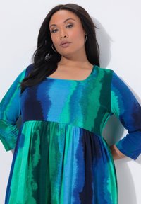 Langærmet kjole med firkantet halsudskæring, lavet af et glat stof med blå og grønne akvarelstriber, udvidet design ved taljen.