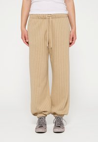 Beige, ribbelachtige joggingbroek met een elastische tailleband en een trekkoord, met geribbelde hemden en een relaxte pasvorm. Gecombineerd met grijze sneakers.