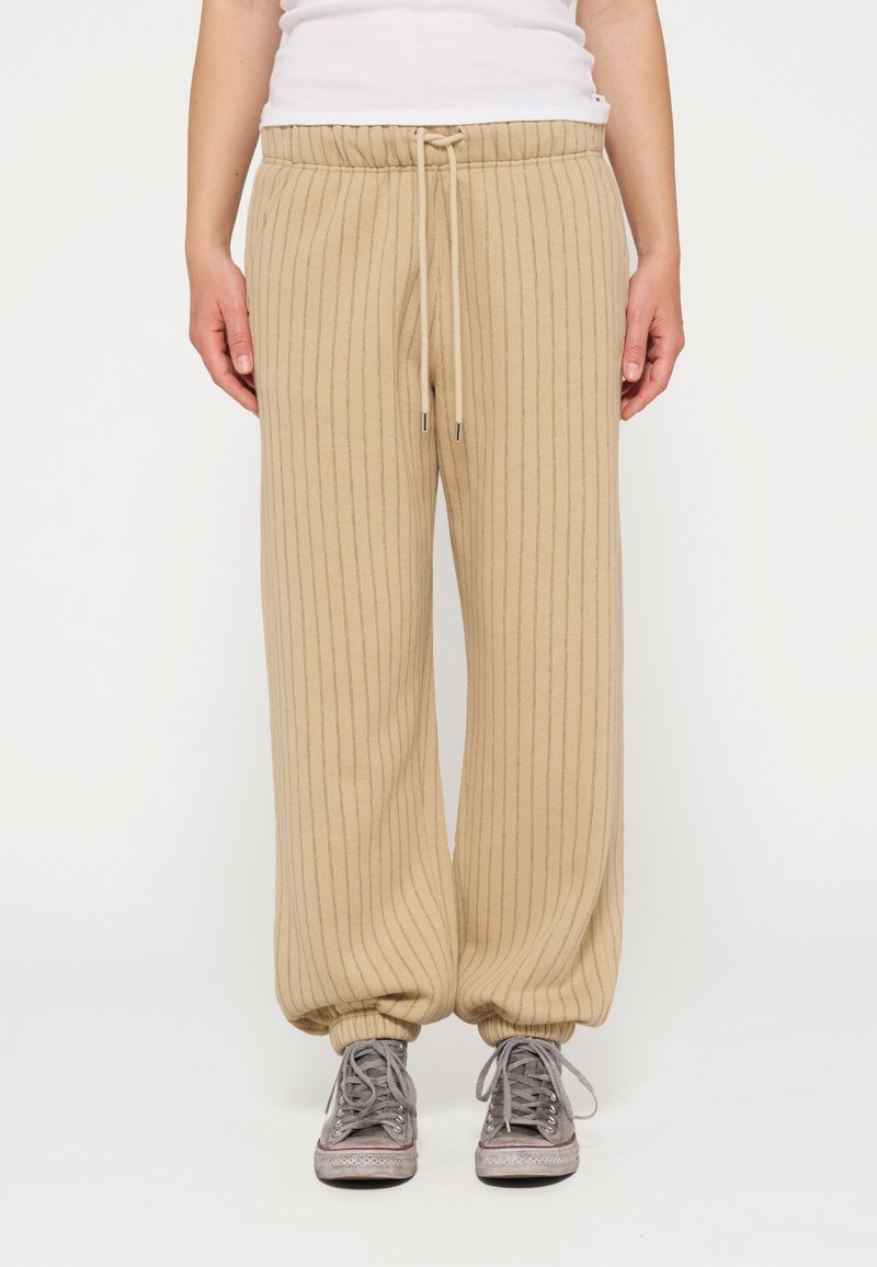 Beige, ribbelachtige joggingbroek met een elastische tailleband en een trekkoord, met geribbelde hemden en een relaxte pasvorm. Gecombineerd met grijze sneakers.