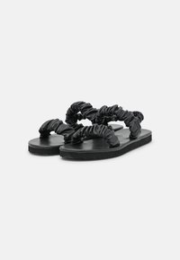 Black sandals with two ruched straps, flat sole, and a textured footbed. Made from smooth material, featuring a minimalist design.