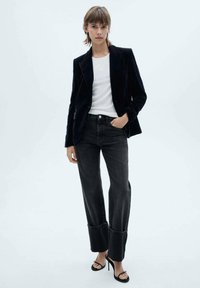 Satin sort blazer, hvid skjorte, mørke denim jeans med opsmøg, og sorte stiletter; minimalistisk design og rene linjer.