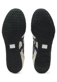 Suole delle sneakers con un motivo in gomma nera testurizzata, con sezioni superiori beige e blu navy. Dettaglio del logo sul lato di ciascuna suola.