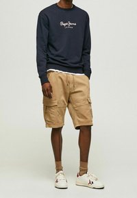 Navy crew neck sweatshirt with white "Pepe Jeans London" logo, paired with tan cargo shorts featuring multiple pockets and drawstring waist. White sneakers.