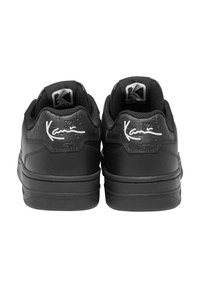 Sorte sneakers med overdel af struktureret læder, polstret krave og gummisål. Har hvid signaturdetalje på bagsiden.