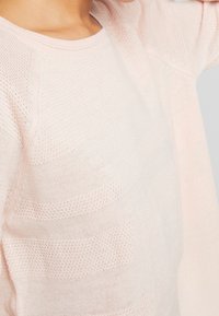 Hellrosa gestrickter Pullover mit einer strukturierten Musterung, rundem Ausschnitt und Raglanärmeln, der verschiedene Strickmuster zeigt.