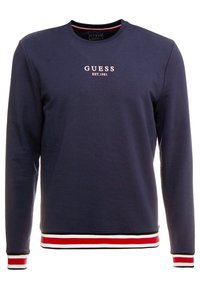 Námořnická modrá mikina s dlouhými rukávy, žebrovanými manžetami a lemem, která má červené, bílé a černé pruhy. Vyšívané logo "GUESS EST. 1981".